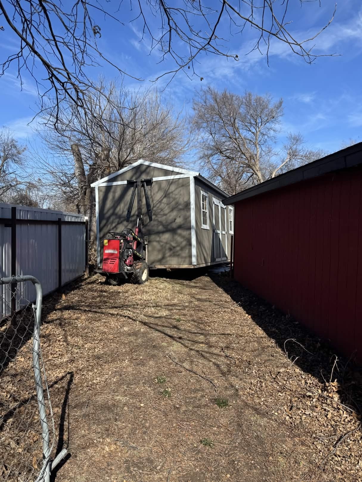 Shed being delivered through a tight backyard between a metal fence and existing building using a shed mule
